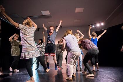 En grupp människor dansar barfota på en scen med armarna i luften i olika rörelser.