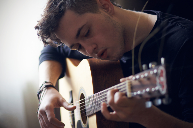 Ung man spelar akustisk gitarr och tittar koncentrerat på strängarna.