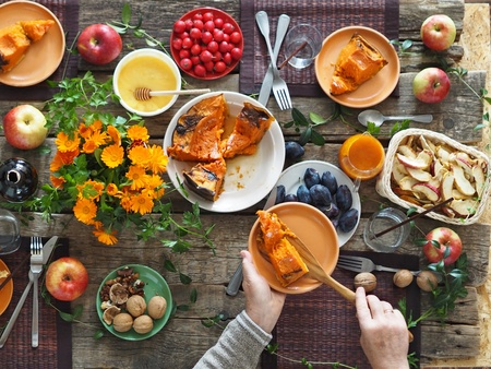 Ett rustikt matbord med paj, frukt, nötter, blommor och två händer som serverar paj.