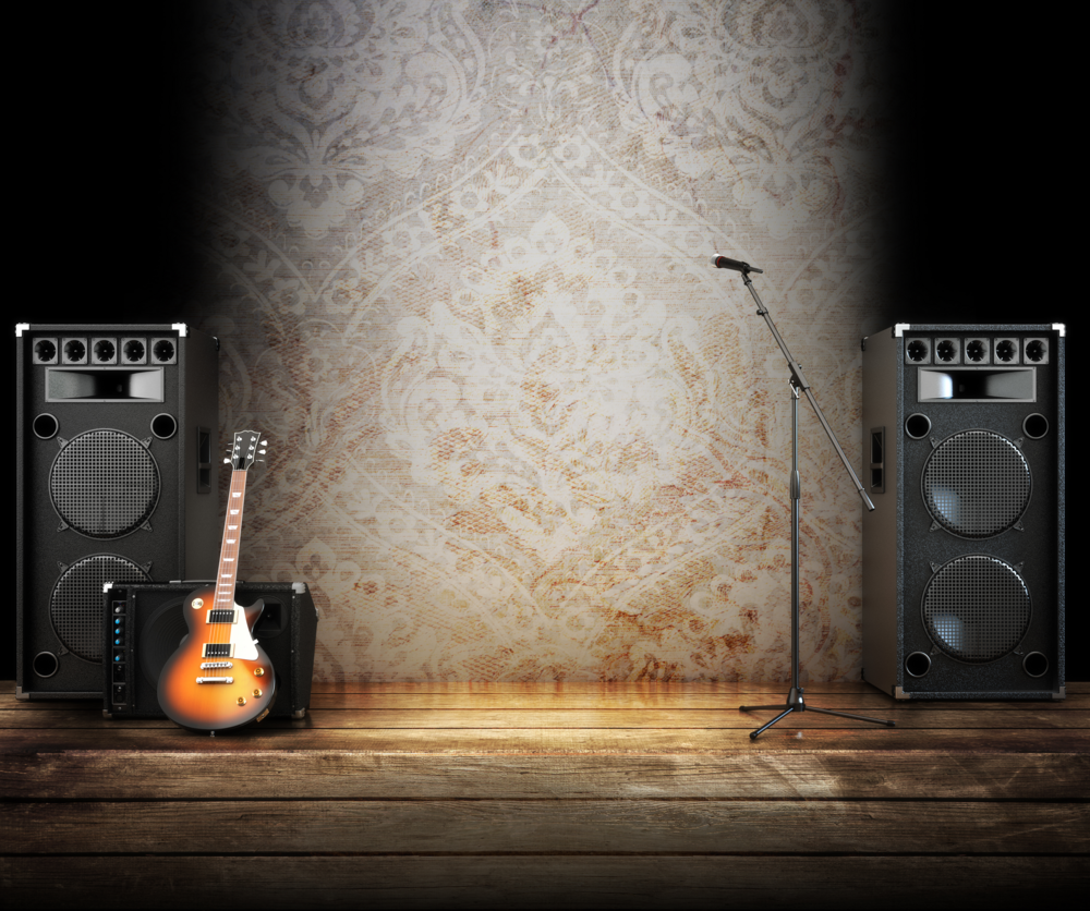 En tom scen med två stora högtalare, en elgitarr på förstärkare och en mikrofon på stativ.