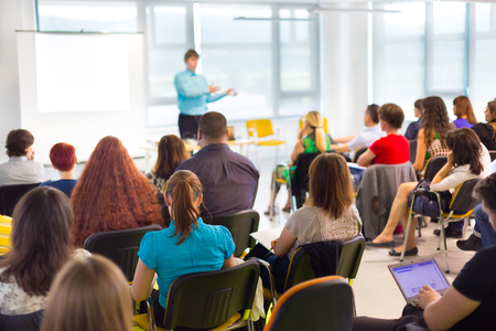 En grupp människor sitter i ett klassrum och lyssnar på en person som håller en presentation vid en whiteboard.