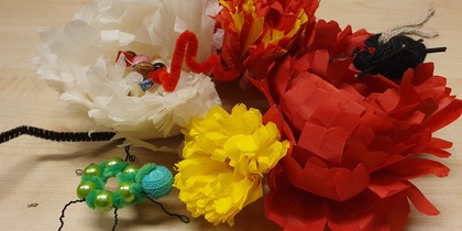 Färgglada pappersblommor och små insekter av pärlor och piprensare på ett träbord.
