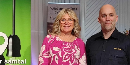 Två personer står bredvid en grön skylt med texten 'Plats för samtal'.