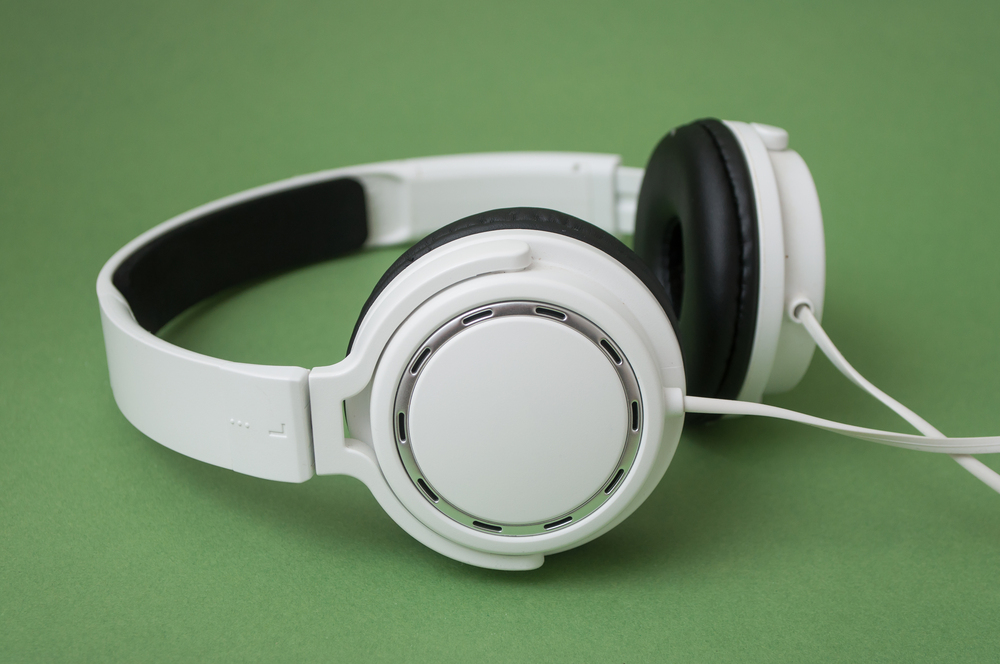 Vita hörlurar med sladd ligger på en grön bakgrund.
