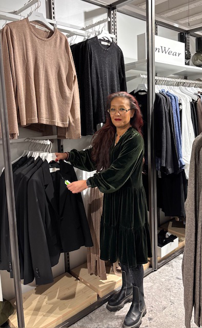 En person i grön sammetsklänning tittar på svarta kavajer i en klädbutik.