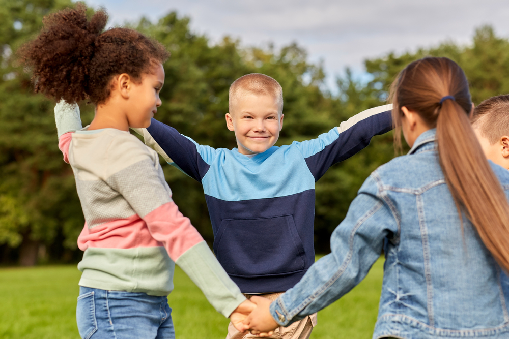 Fyra barn leker tillsammans utomhus på en gräsmatta, håller varandra i händerna.