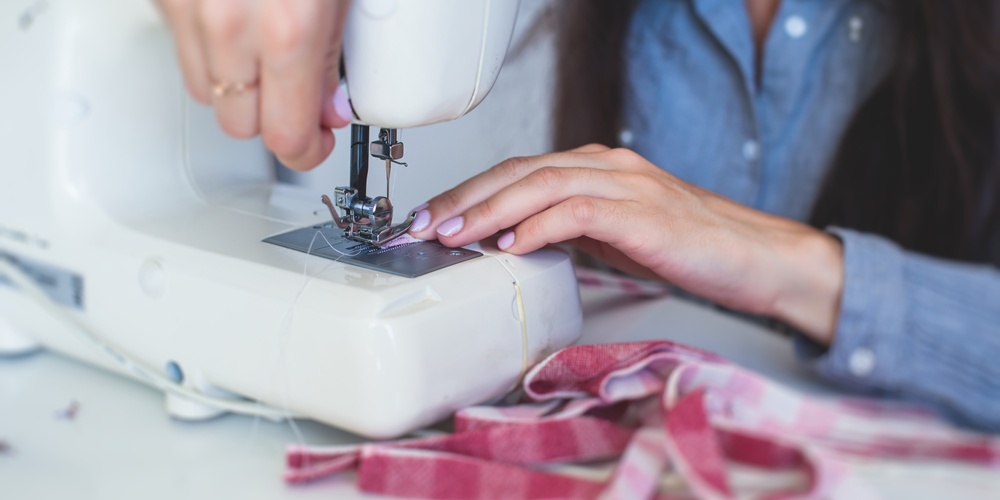 En person syr tyg med en symaskin, händerna syns tydligt vid arbetet.