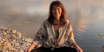 Kvinna sitter i meditationsställning på en brygga vid en sjö i solnedgången.