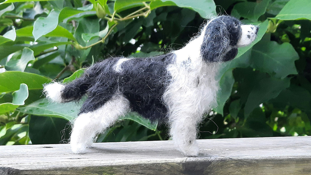 En filtad hundfigur i svart och vitt står på en träyta med gröna blad i bakgrunden.