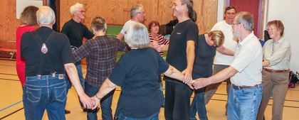 En grupp vuxna håller varandra i händerna och dansar i en ring i en gympasal.