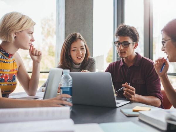 Fyra unga personer sitter samlade kring en laptop.