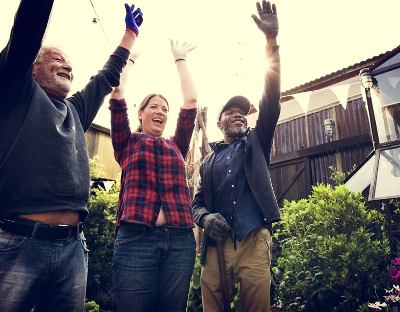 Tre personer står utomhus och lyfter sina händer i luften.