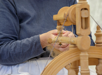 Person spinner garn med en gammaldags spinnrock, fokus på händer och verktyg.
