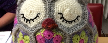 Virkad uggla i färgglada mormorsrutor står på ett bord, med slutna ögon och blomliknande mönster.