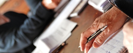 Flera personer sitter vid ett bord och skriver i anteckningsblock med papper och pennor.