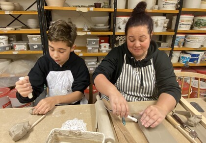 En pojke och en kvinna arbetar med lera vid ett bord i en keramikverkstad.