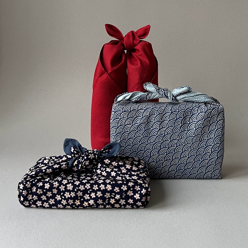 Tre paket inslagna i tyg med japansk furoshiki-teknik, i rött och blått mönstrat tyg.