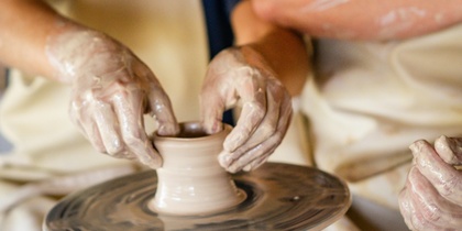 Två personer arbetar tillsammans med att forma lera på en drejskiva.
