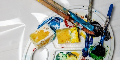 En konstnärspalett med färgglada färger, penslar och svampar på en vit bakgrund.