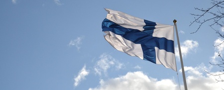 Finlands flagga vajar mot en blå himmel med några moln.
