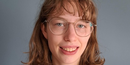 Person med axellångt brunt hår och blommig rödvit tröja mot grå bakgrund. Ansiktet är suddat.