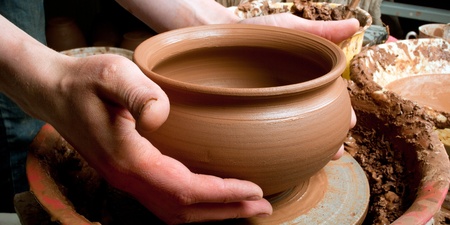 Två händer formar en lerkruka på en drejskiva i en keramikverkstad.