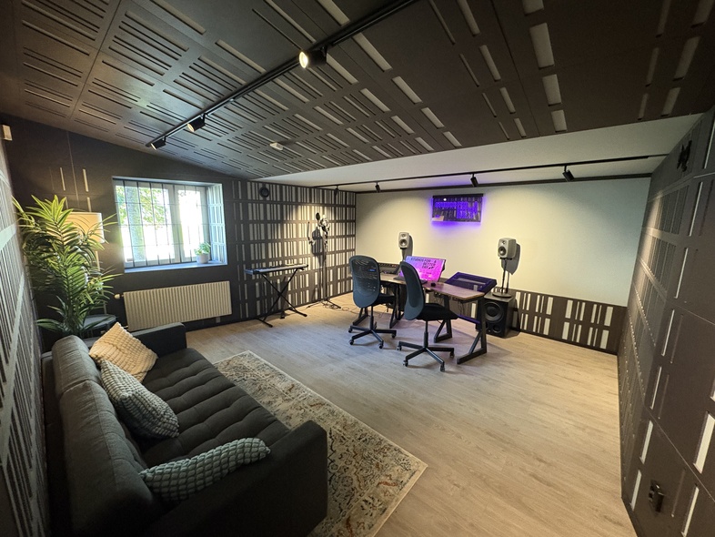 Modernt musikstudio med akustikpaneler, soffa, skrivbord, högtalare och mikrofon.