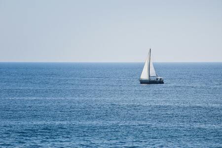 En segelbåt med vita segel seglar ensam på ett lugnt blått hav under en klar himmel.