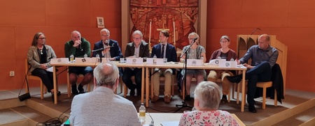 Ett panelmöte med nio personer vid ett bord i en kyrksal, två personer sitter vända mot panelen.