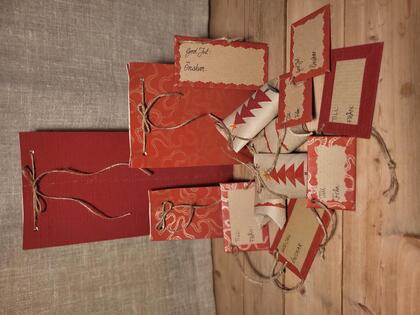 Handgjorda julklappsetiketter och presentförpackningar i rött och brunt med snören på ett träbord.