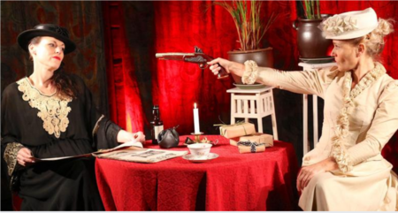 Två kvinnor i vintagekläder sitter vid ett bord, en riktar en pistol mot den andra.