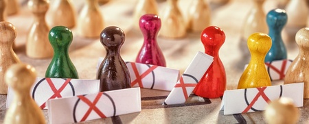 Färgade spelpjäser står i en grupp omgivna av barriärer med röda kryss, fler pjäser i bakgrunden.