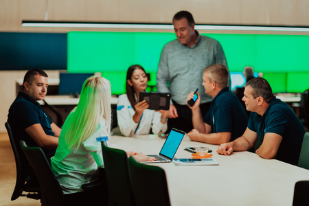 En grupp människor sitter runt ett konferensbord och diskuterar med laptops och surfplattor.
