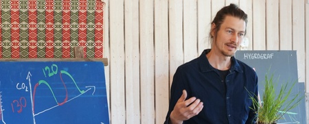 Man håller en krukväxt och föreläser vid en griffeltavla med grafer och temperaturer.