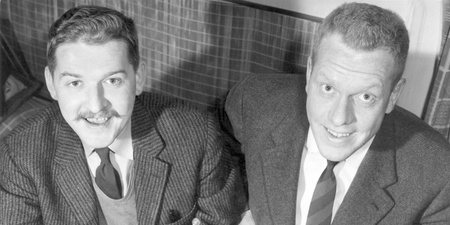 Två män i kostym sitter bredvid varandra och håller i ett schackbräde med pjäser.