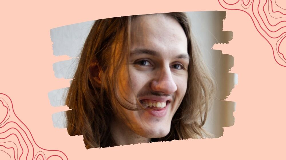 Person med långt brunt hår står mot en ljus bakgrund med rosa och vita detaljer.