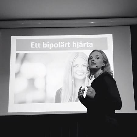 En person håller en presentation framför en projektor med texten 'Ett bipolärt hjärta'.
