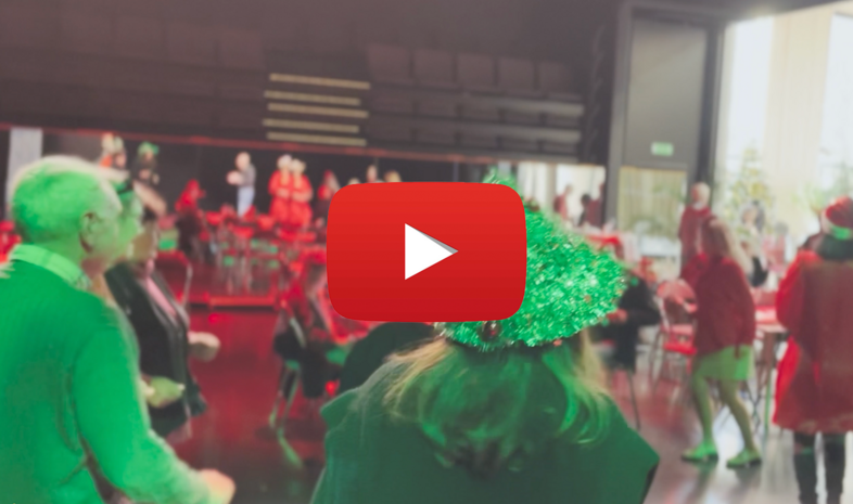 Personer i julkläder dansar i en sal med röda stolar och dekorationer. En stor YouTube-spelknapp syns i mitten.
