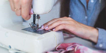 En person syr tyg med en symaskin, händerna syns tydligt vid arbetet.