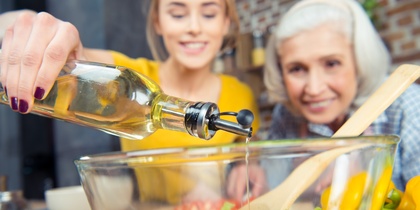 Två kvinnor lagar mat tillsammans och häller olja i en salladsskål med grönsaker.