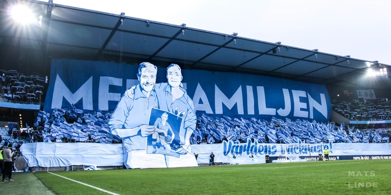 Stor banderoll på fotbollsläktare med två tecknade personer och texten 'MFF FAMILJEN'.