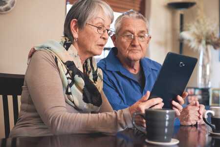 Två äldre personer sitter och tittar tillsammans på en iPad.