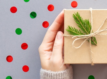 Två händer håller ett inslaget paket med snöre och grankvist mot en bakgrund med röda och gröna prickar.