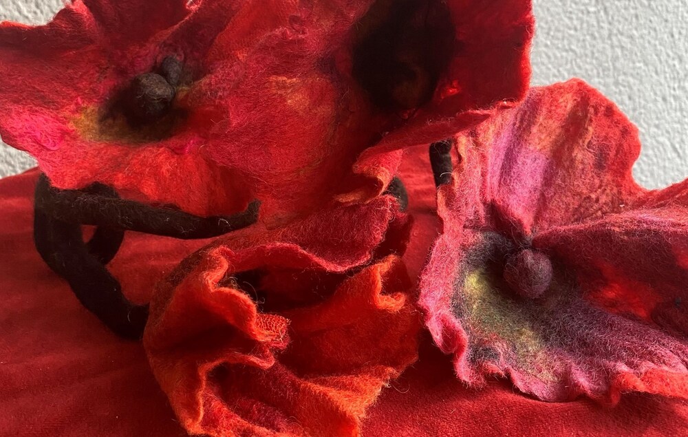 Närbild på röda filtade blommor placerade på ett rött tyg, mot en ljus bakgrund.