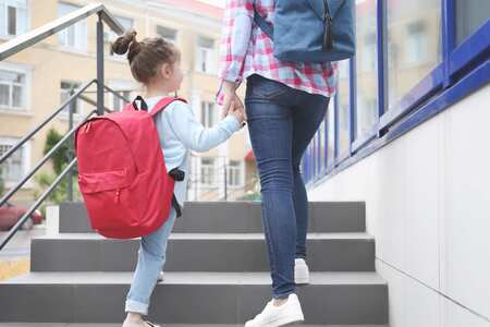 Ett barn med röd ryggsäck går upp för en grå trappa och håller ett barn i handen.