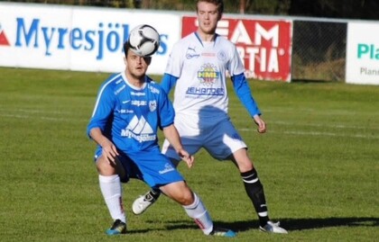 Två fotbollsspelare tävlar om bollen på en gräsplan under en match.