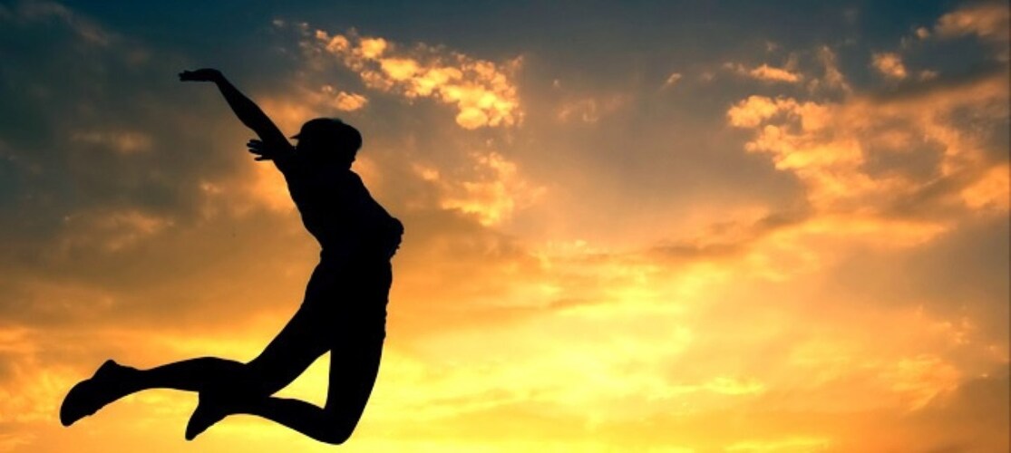 En person hoppar i luften mot en färgstark solnedgång med siluett mot himlen.