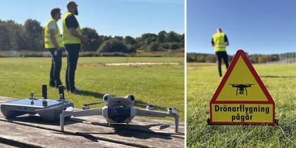 Två personer i reflexvästar styr en drönare på en gräsplan, med en varningsskylt om drönarflygning.