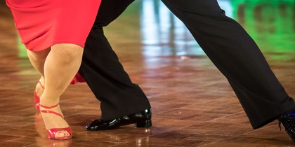 Två personer dansar tillsammans på ett dansgolv, endast deras ben och fötter syns.