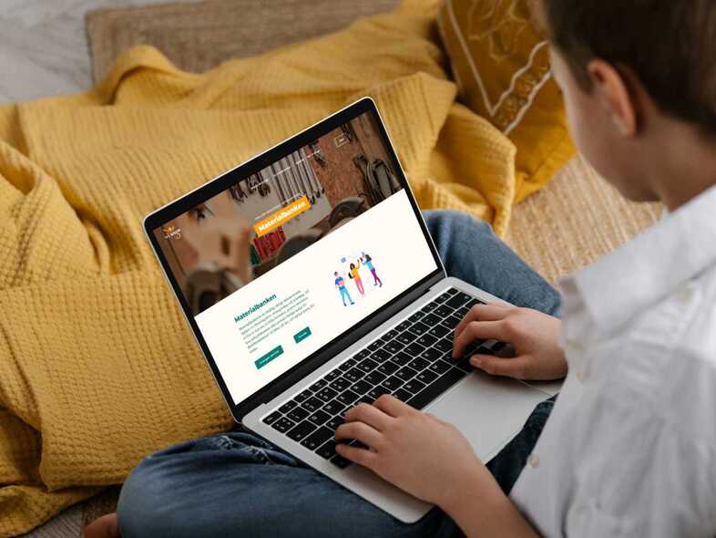 Ett barn sitter på en säng och skriver på en laptop som han har i knät.